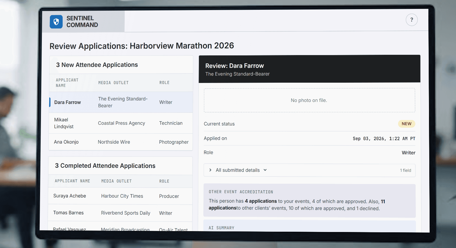 A monitor on an office desk showing the application review queue: three new applications listed by surname, with one open alongside its status, submitted answers, and a count of the applicant's accreditations at other events.